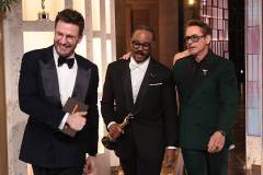 HOLLYWOOD, CALIFORNIA - MARCH 15: In this handout photo provided by The Academy, presenters Chris Evans (L) and Robert Downey Jr. (R) walk off stage as Ryan Coogler carries the Writing (Original Screenplay) award for "Sinners" during the 98th Oscars at Dolby Theatre on March 15, 2026 in Hollywood, California. (Photo by Al Seib / The Academy via Getty Images)